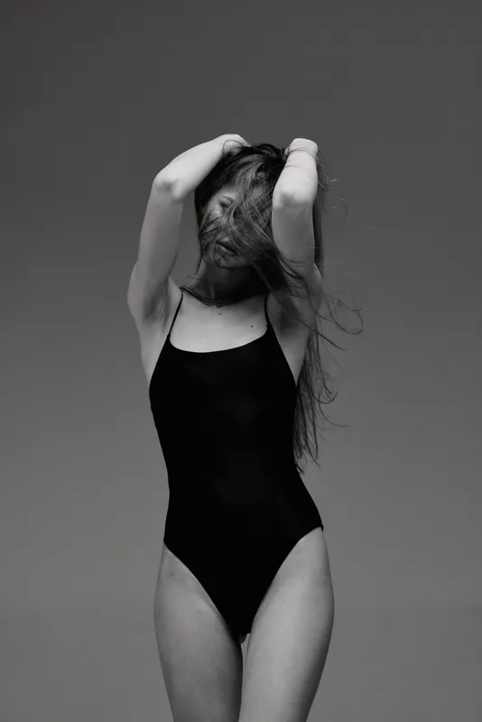 Black and white portrait of a woman in a black swimsuit with flowing hair expressing freedom and grace.