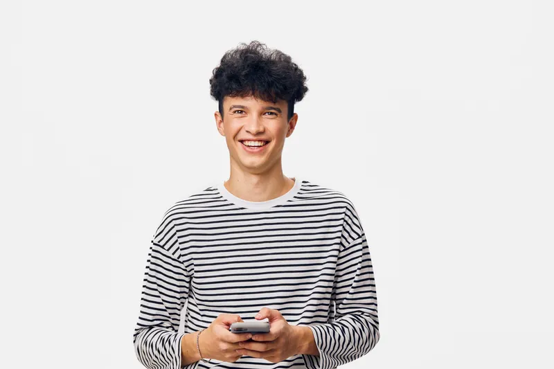 smiling young man in striped shirt holding smartphone, isolated on white background, casual style, short curly hair, positive expression