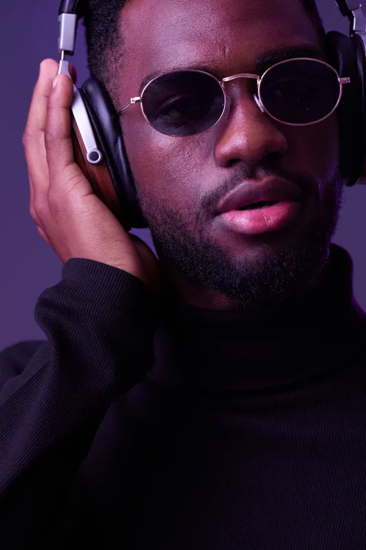 Stylish man with headphones wearing sunglasses, showcasing confident emotions against a vibrant purple background, perfect for music and lifestyle themes