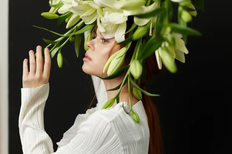 Elegant woman with floral headpiece, wearing a white sweater, showcasing emotions of tranquility and creativity against a dark background