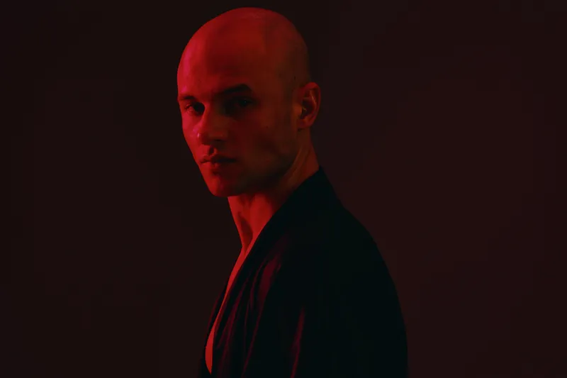 Intense man portrait in dramatic red lighting, showcasing strong emotions with a powerful gaze. A striking contrast highlighting the subject’s features.