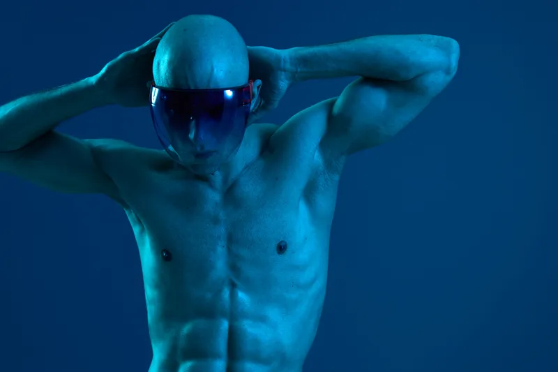 Athletic man posing with a futuristic look and a blue background, showcasing strength and confidence in a vibrant color light image.