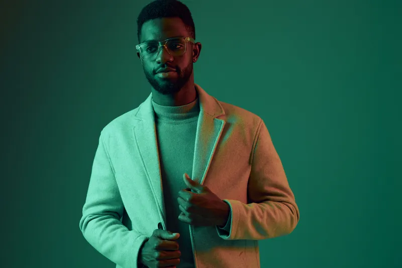Stylish African man in modern chic attire posing against a green background, showcasing confidence and sophistication