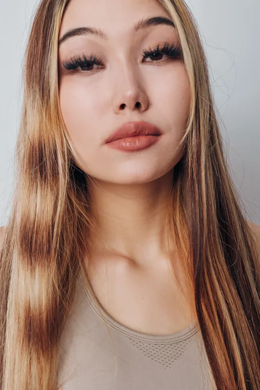 Young woman with long hair and natural makeup posing with neutral expression in studio. Closeup portrait of female model with smooth skin and casual clothing for beauty concept.
