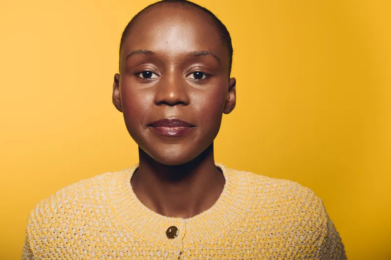 Close-up portrait of confident dark skinned African woman with shaved head wearing yellow sweater against bright yellow background. Concept of beauty, empowerment, and diversity.
