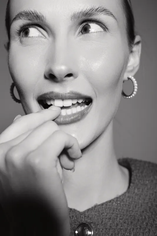 Close up of white woman with light skin smiling and biting finger in thoughtful expression on plain background.