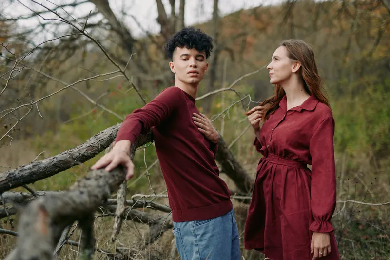 A candid, authentic moment between two people outdoors, with natural light and sincere expressions, capturing genuine connection as they lean on a wooden fence amid autumn brush.