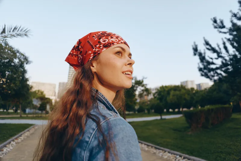 Lifestyle woman wearing modern boho-western denim street style with a red bandana, enjoying an outdoor urban setting in warm film color tones.