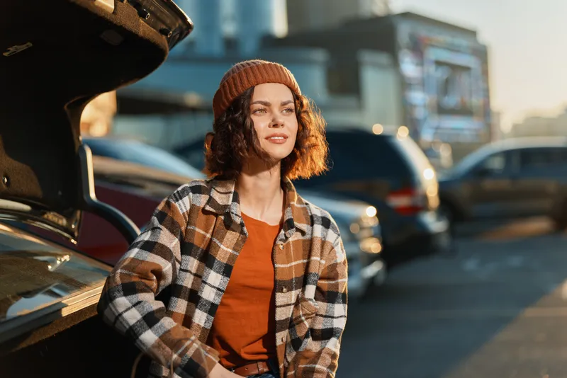 Woman, car, parking, golden, candid, lifestyle young woman in beanie and plaid jacket leaning on an open trunk in warm golden hour glow, authenticity, mindful living and emotional storytelling.