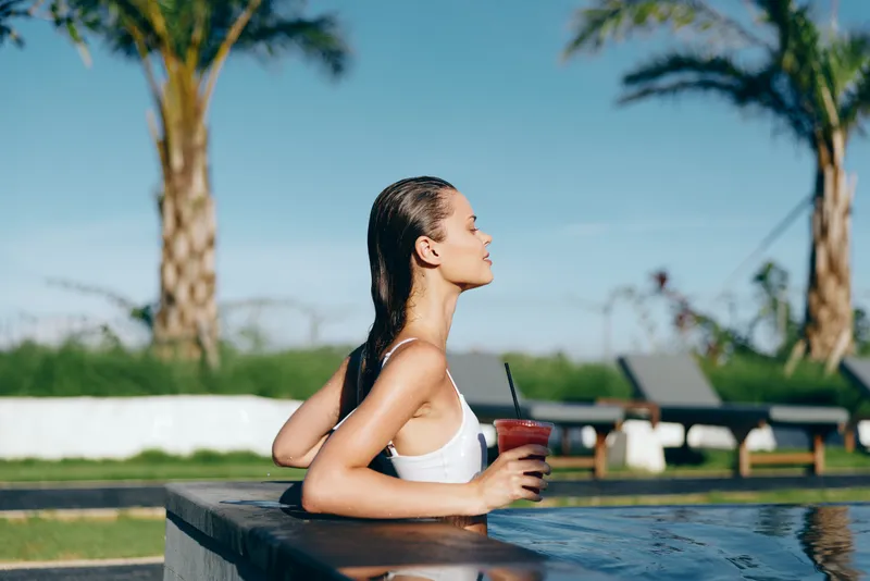 woman by pool outdoors enjoying leisure in sunny relaxation, a cheerful summer lifestyle moment with happy casual vibe, sunlit water reflections and warm colors framing a serene poolside scene