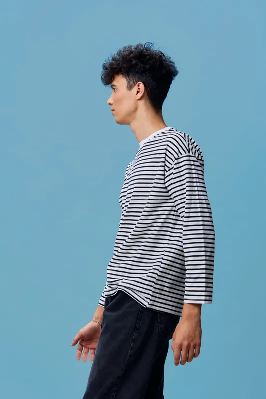 Young man wearing a striped long-sleeve shirt stands against a blue background, showcasing casual style and modern fashion with a thoughtful expression.