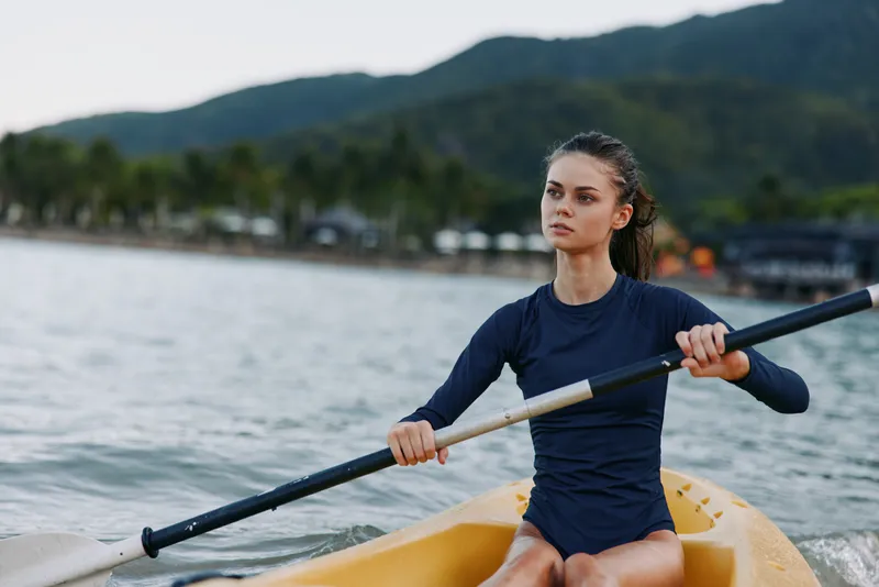 Female kayaker paddling alone in a bright yellow kayak on calm water, showcasing strength, balance, and focus during an outdoor paddling session.