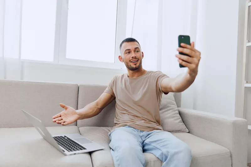 Happy man video calling from home, embracing emotional moments and authenticity amidst the challenges of modern life, reflecting soft masculinity and self-discovery.