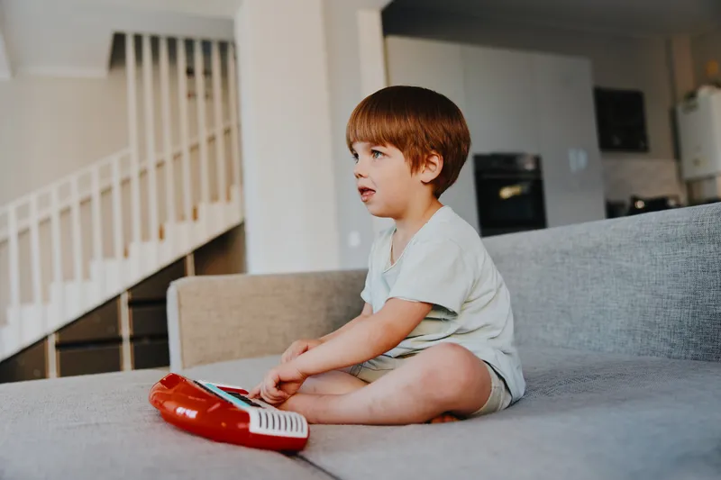 Curious boy playing a toy keyboard in a cozy living room, showcasing creativity and joy in a relaxed setting. Perfect for family-related themes.