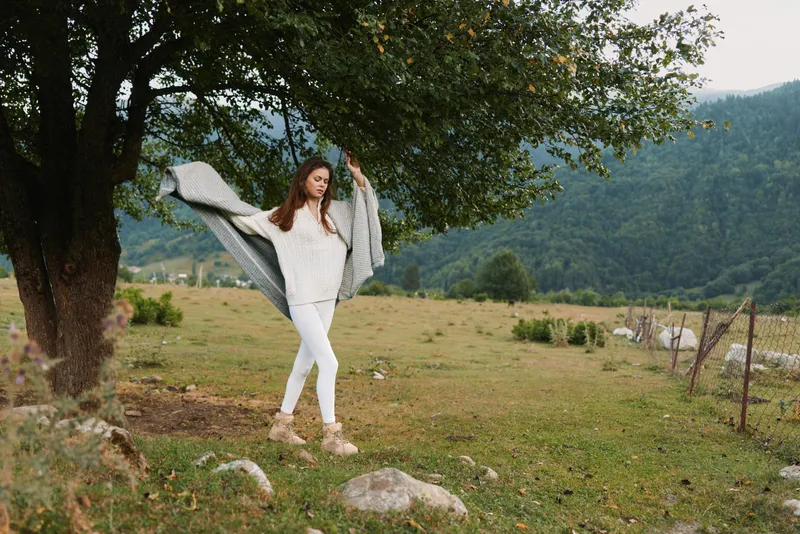 Young woman in white outfit posing outdoors under a leafy tree in a rural field. Lifestyle photography showing freedom, nature, and calm, with soft daylight and relaxed movement.