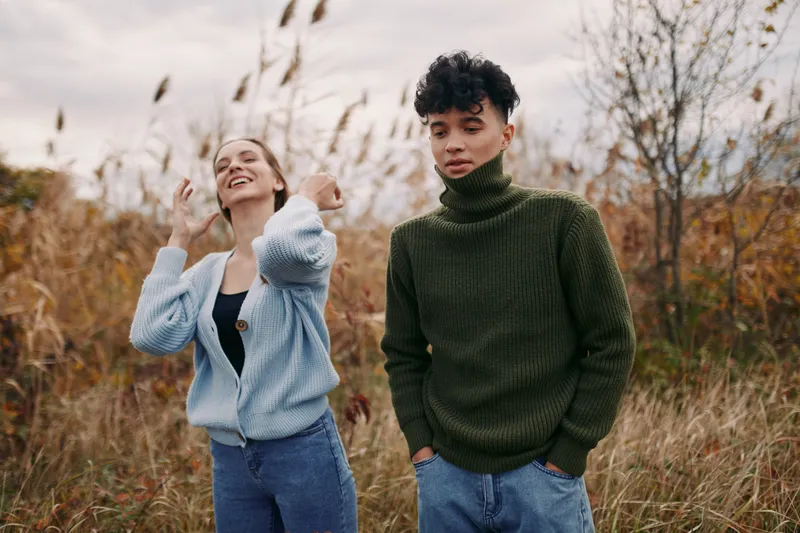 Two young adults stand in a windswept autumn field, captured in a candid, authentic moment that highlights genuine emotion, natural interaction and visual credibility and quiet atmosphere.