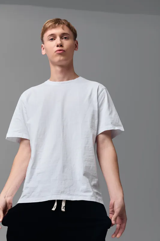 Man in a white t shirt stands confidently from a low angle, showcasing casual fashion and minimal style for lifestyle, apparel and model photography