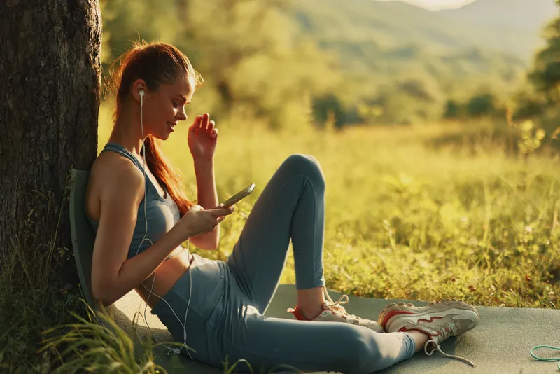 Young woman in activewear listening to music outdoors, showcasing fitness and leisure in a vibrant natural setting, ideal for promoting a healthy lifestyle and wellness