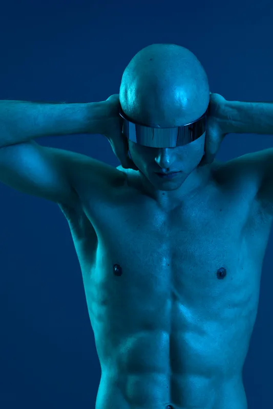 A bald man in futuristic sunglasses, showcasing a striking blue tone, exhibits a sense of introspection and modern aesthetics in this captivating image.