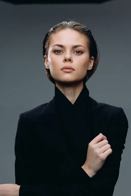 Confident woman in black turtleneck with intense gaze and neutral grey background