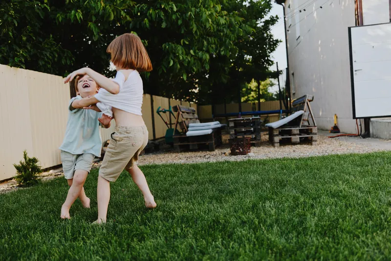 Two joyful children playing together in a green backyard, full of laughter and energy, capturing the essence of childhood fun and outdoor activities. ### ???????? ??????? ???????? (DESCRIPTION2):