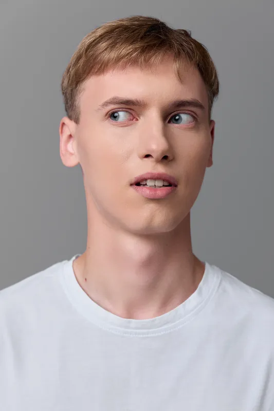 Young man in a white t shirt, looking to the side with a thoughtful expression, studio shot on a neutral gray background, clean and modern mood for fashion, lifestyle and modeling projects