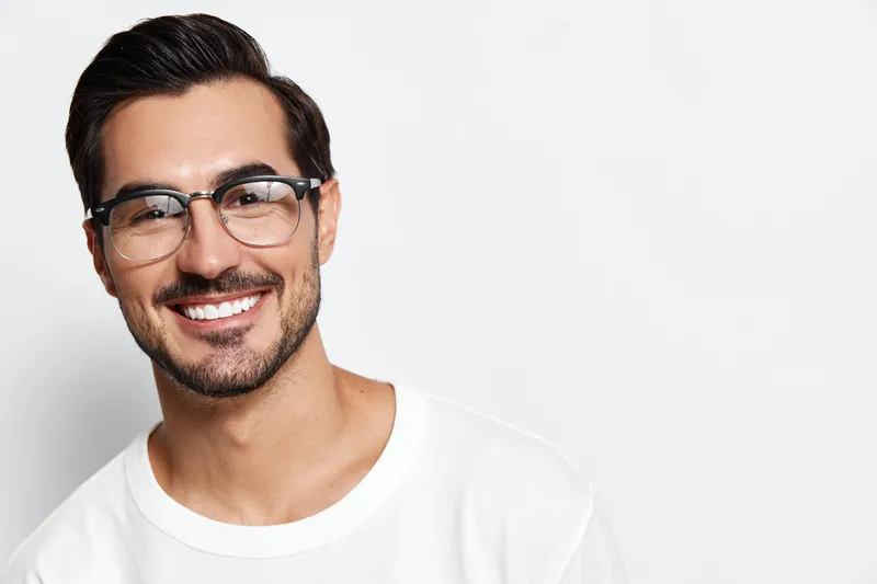 Smiling man wearing glasses and a white t-shirt, looking at the camera with a friendly expression against a plain light background. People lifestyle concept.