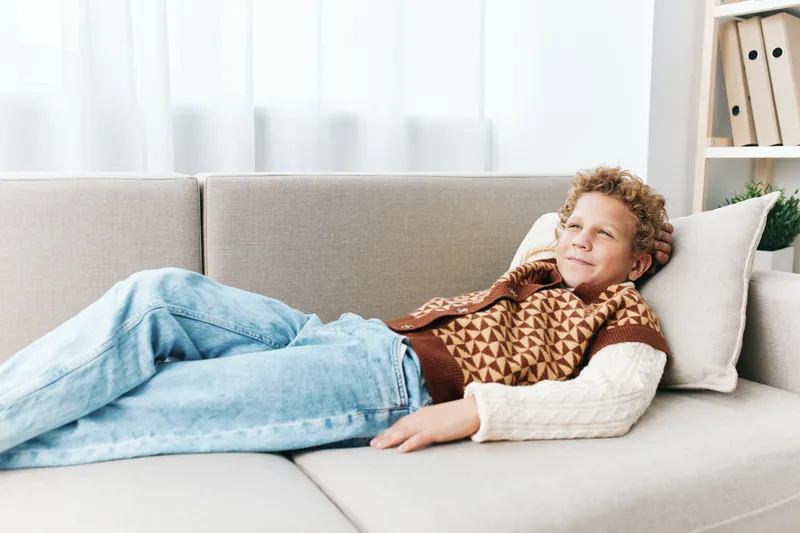 An authentic lifestyle scene featuring a child resting on a sofa in casual attire, reflecting school play and home comfort in a candid, everyday moment.