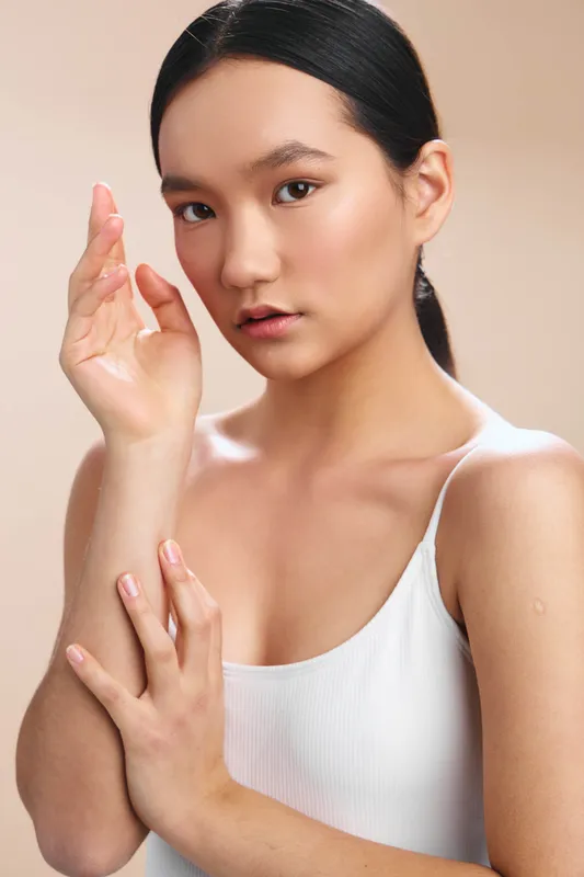 asian woman portrait in studio lighting wearing a white tank top. The calm expression and soft pose convey simplicity, focus, and natural beauty in a minimal setting.