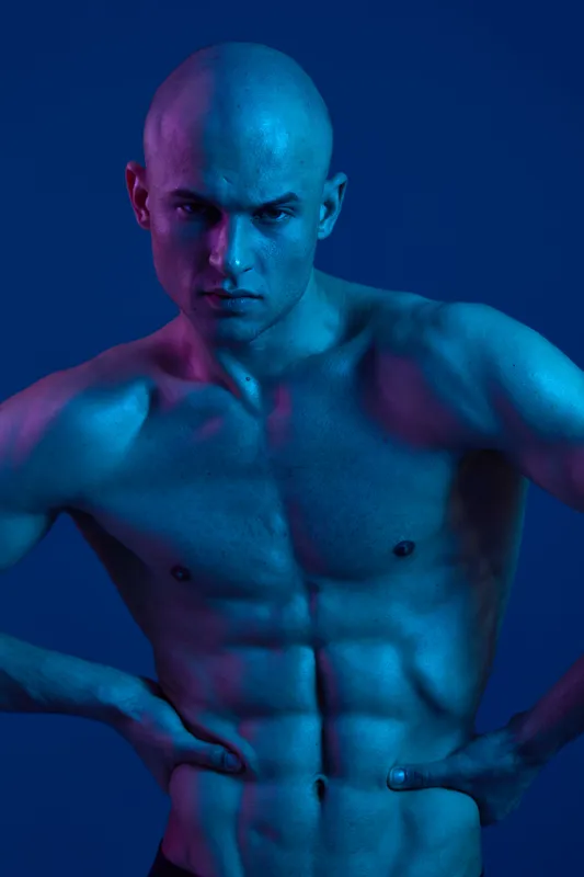 Captivating image of a man with a muscular build, showcasing vibrant blue and purple lighting that enhances his features in a stunning black and white composition.