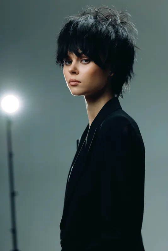 Young woman with modern short haircut wearing black outfit in studio with muted background and soft lighting