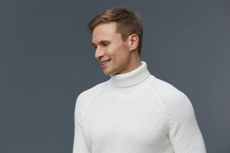smiling caucasian man in white turtleneck sweater looking side isolated on gray background casual wear digital nomad concept