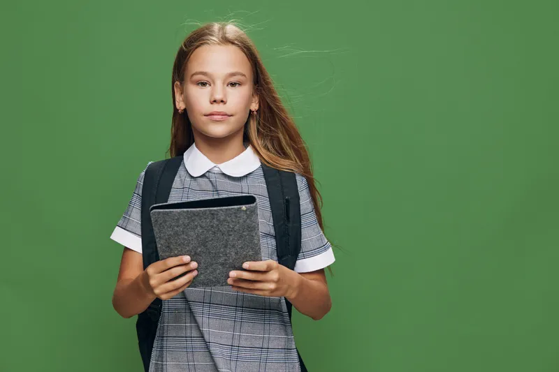 Girl student with backpack holding tablet digital device for education and learning, casual school uniform and technology in classroom or study environment.