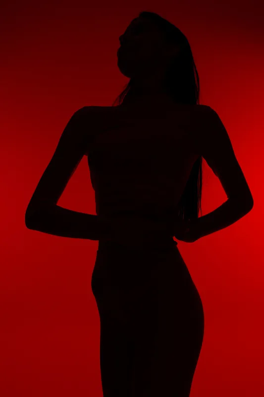 Silhouetted woman sport fitness pose with hands on hips against vivid red background, highlighting athletic figure and strength in dynamic lighting.
