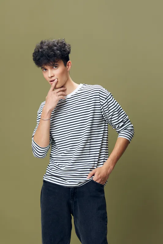 young man in striped shirt posing thoughtfully with finger near lips against muted olive background, casual style and contemplative mood