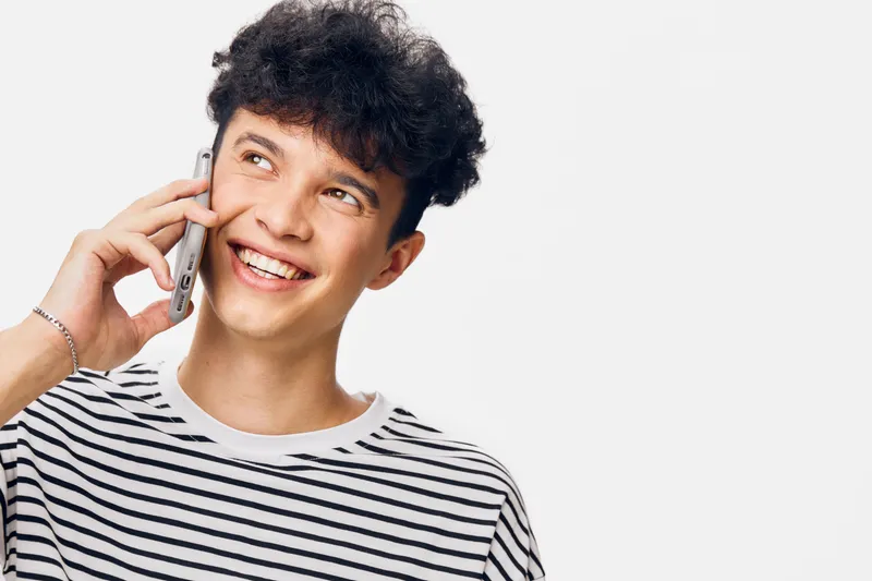 smiling man talking on smartphone, casual striped shirt, young adult with curly hair, bright expression, isolated white background, positive mood