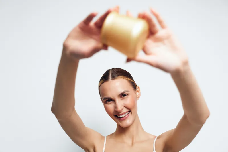 Smiling woman holding cosmetic jar above head, clear skin, natural light, white background, beauty concept, skincare routine, healthy lifestyle, joyful expression, clean design
