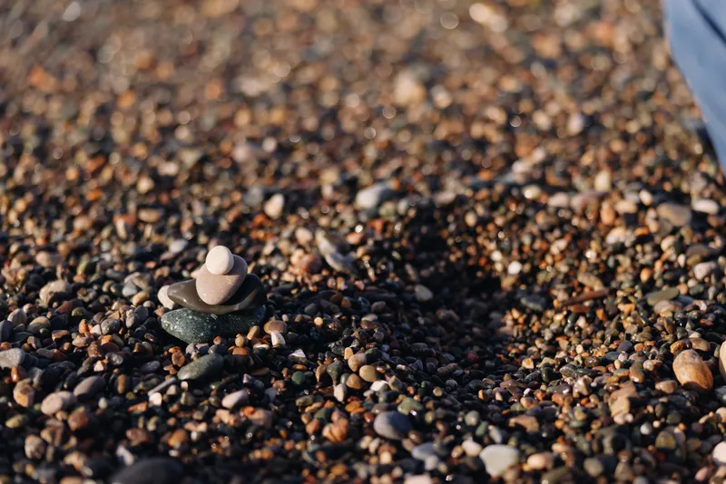 Stone, pebble, balanced stack on a beach with textured gravel and soft coastline, a tiny cairn rising among varied pebbles, capturing calm nature and rugged detail.