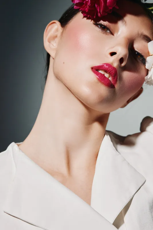 Portrait of a woman with glossy red lips and dramatic eye makeup wearing a white blazer and red accessories, emphasizing creative beauty and fashion style.
