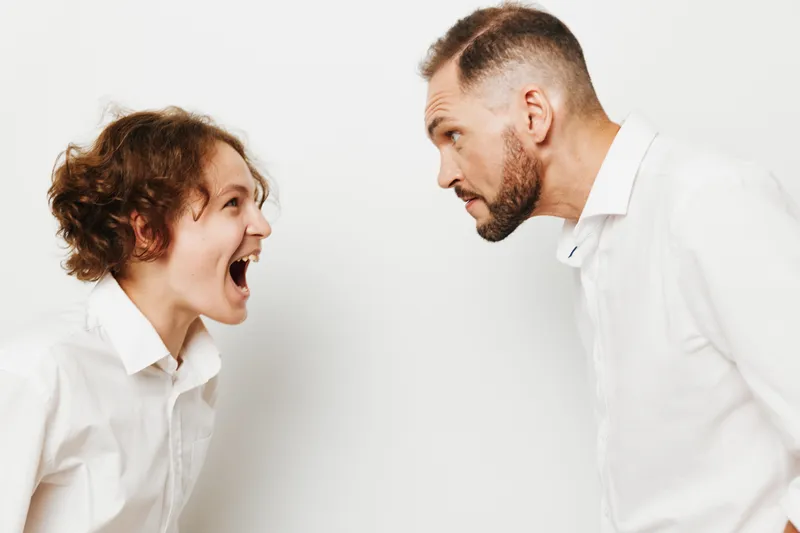 A professional business scene shows two men in white shirts arguing with intensity, standing against an isolated white background, expressing bold emotion and a tense confrontation.
