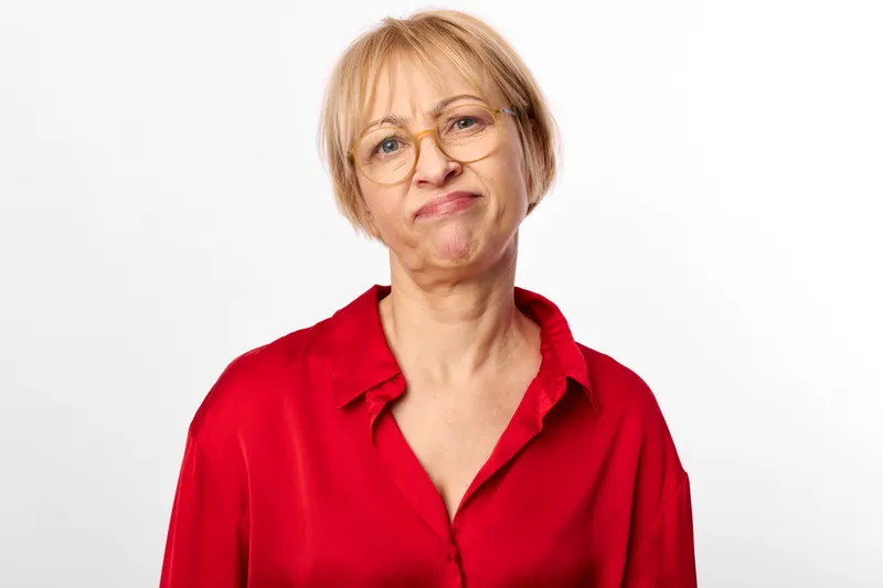 Senior woman portrait in studio, wearing red shirt and glasses, soft face expression, looking at camera, white background, clean minimal composition, calm mood today