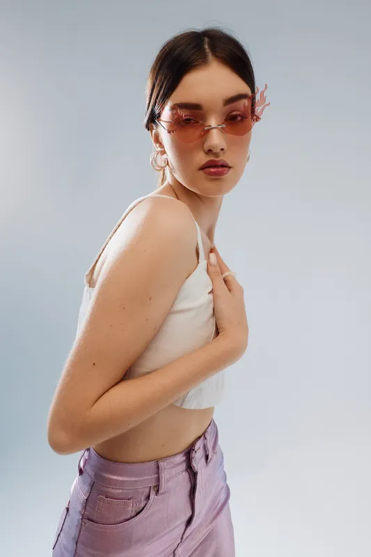 Young woman in stylish pink sunglasses and white crop top poses confidently against a light background. Concept of beauty fashion, style, and modern elegance in portrait photography.