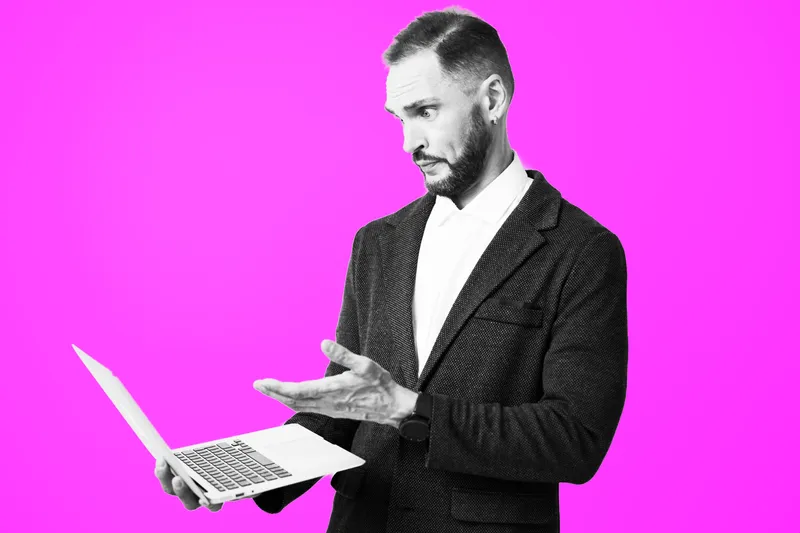 A focused professional man stands against a vibrant colored backdrop, examining ideas on a laptop, projecting confidence, focus, and subtle emotion.