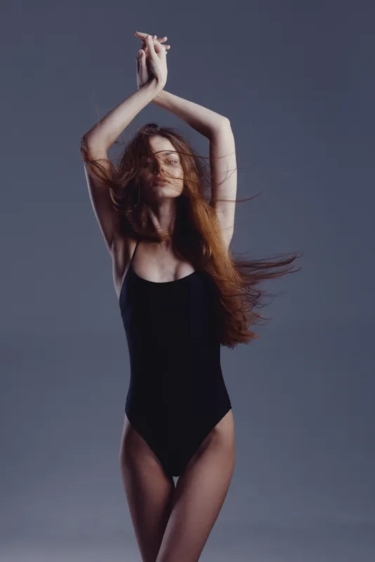graceful woman posing in black bodysuit with flowing hair against gray background