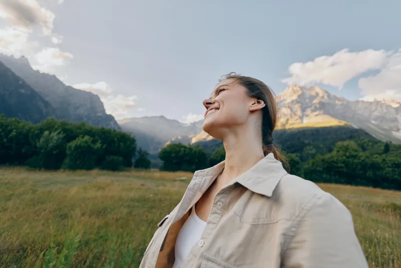 Vibrant outdoor portrait of a woman in a field enjoying nature and mountain views, a carefree mood and smiling expression, capturing lifestyle in a serene moment