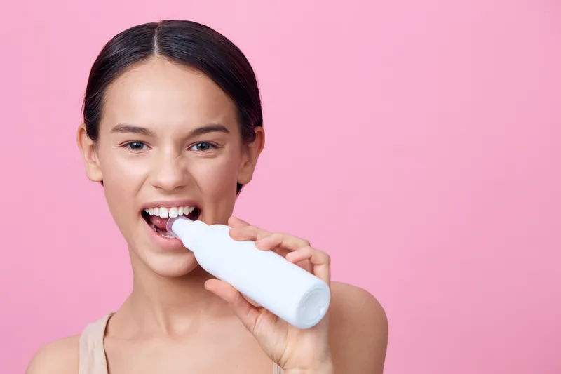 Young woman with healthy smile holding a dental care product against a pink background, expressing joy and confidence in personal care