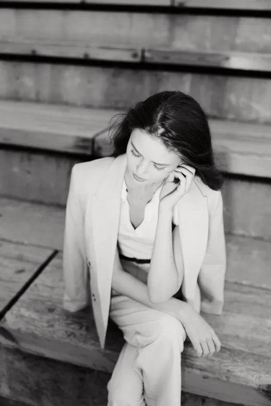 Black and white portrait of a thoughtful woman in light suit sitting on wooden steps, emotional, elegant, casual style, monochrome fashion concept