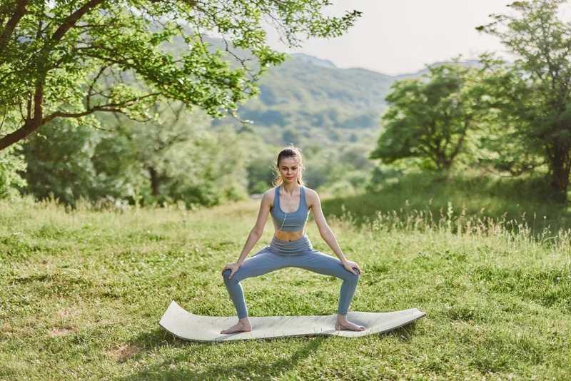Young female athlete performing a yoga pose outdoors in a serene landscape, wearing comfortable athletic wear, showcasing strength and balance in a tranquil green setting