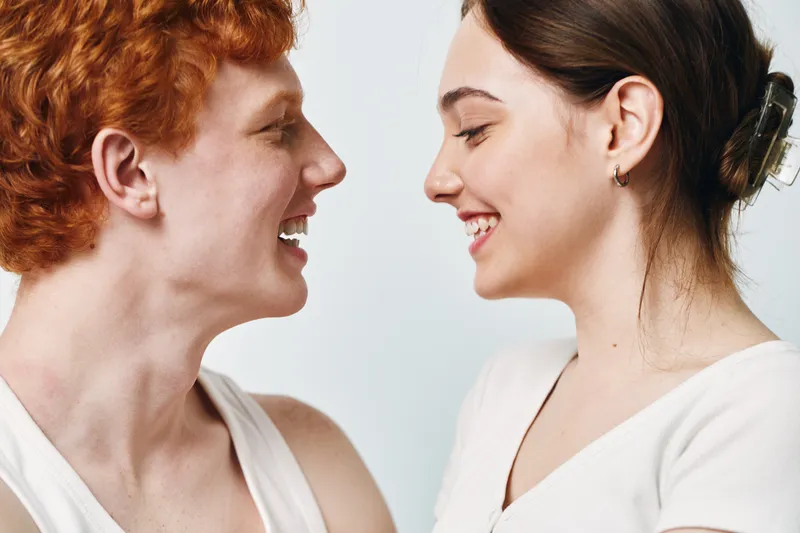 Couple, young man and woman with smile looking at each other on light background. Relationships, happiness and love with casual clothing and natural emotions together.