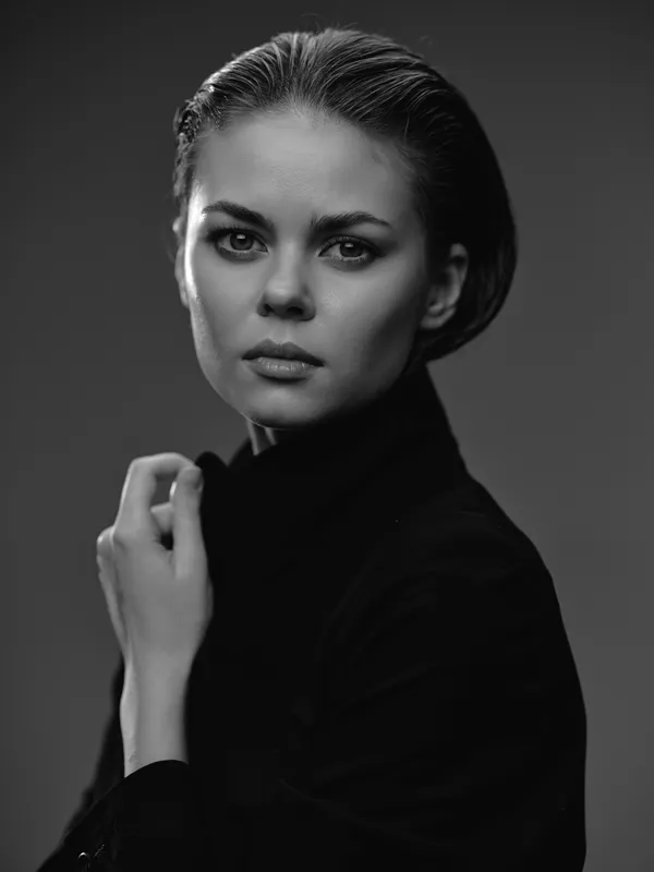 Black and white portrait of a serious woman with short hair in a dark turtleneck, expressing intensity and elegance in studio lighting.